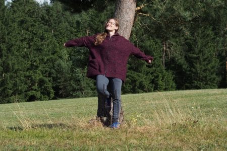 Cornelia Brückner lehnt am Baum mit ausgestreckten Armen vor einem Wald